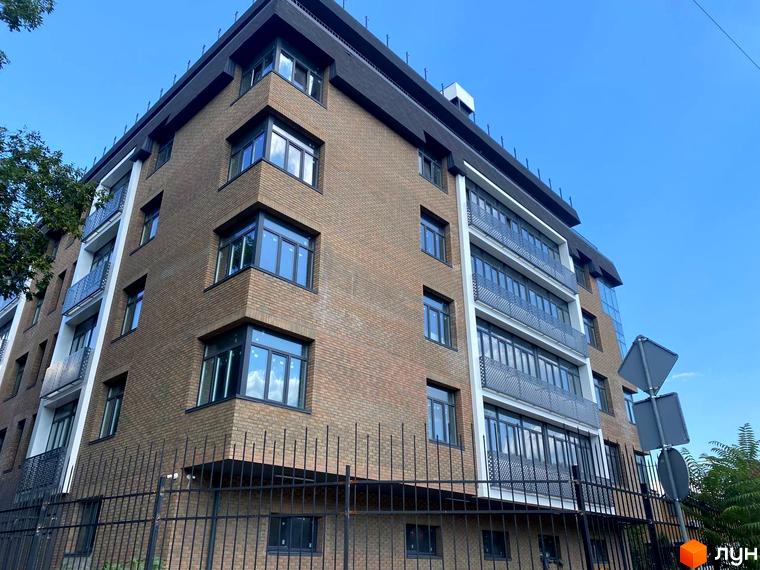 Клубний будинок Donjon з коричневої цегли та великими вікнами на тлі блакитного неба. Огороджена територія з чорною металевою огорожею.