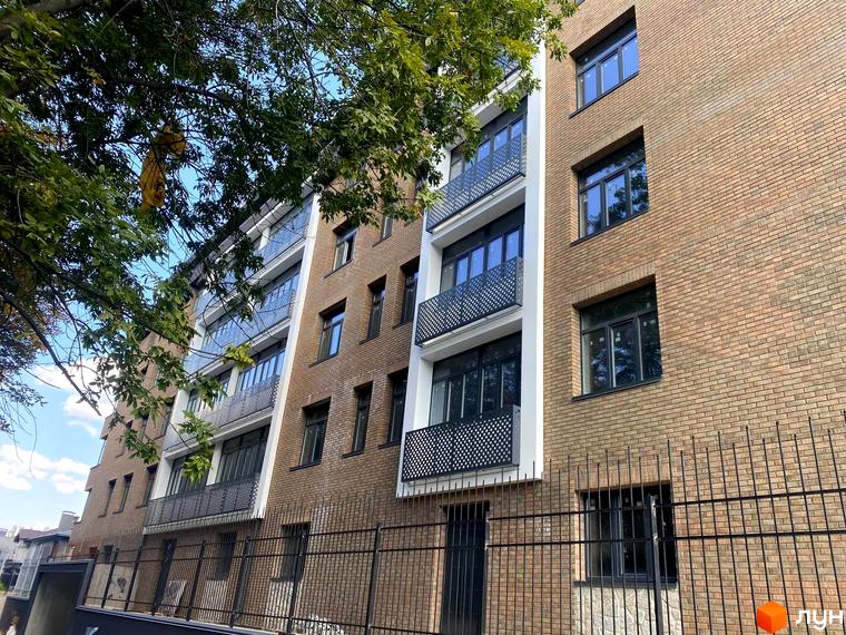 Клубний будинок Donjon з цегляним фасадом та балконами з металевим огородженням, оточений зеленню та огороджений парканом.