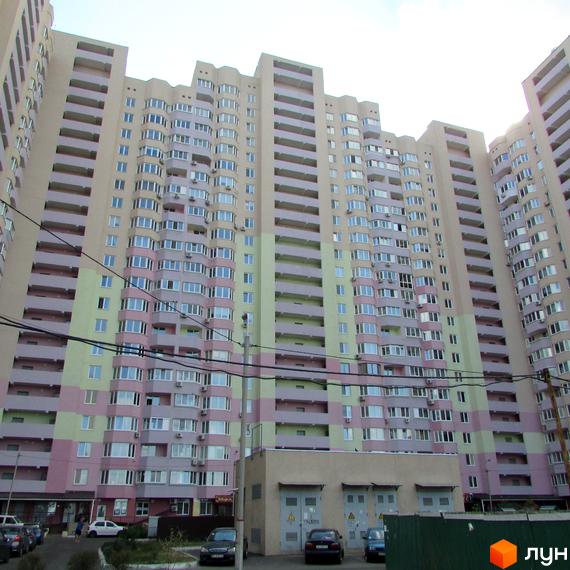 Житловий комплекс Милославичі з фасадом у світлих тонах та балконами. Прибудинкова територія з паркувальними місцями та зеленими насадженнями.