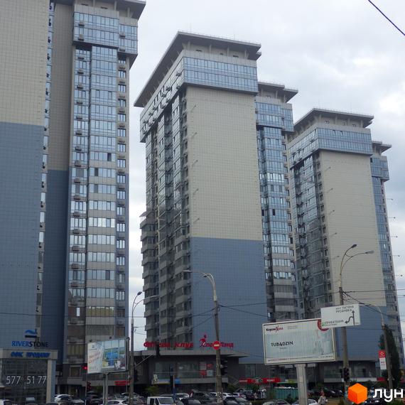 Житловий комплекс RiverStone з високими вежами та скляними фасадами. На першому поверсі розташовані комерційні приміщення. Навколо комплексу видно припарковані автомобілі.