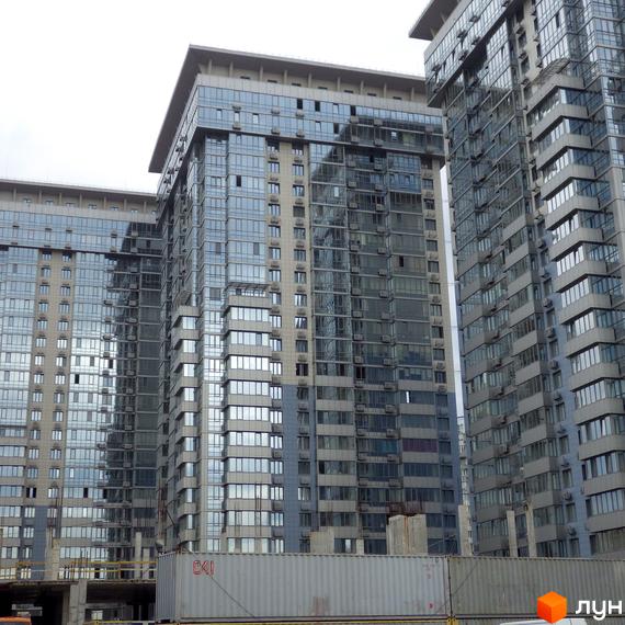 Житловий комплекс RiverStone - це сучасні багатоповерхові будинки з панорамним склінням та кондиціонерами на фасадах. На передньому плані видно будівельні контейнери.