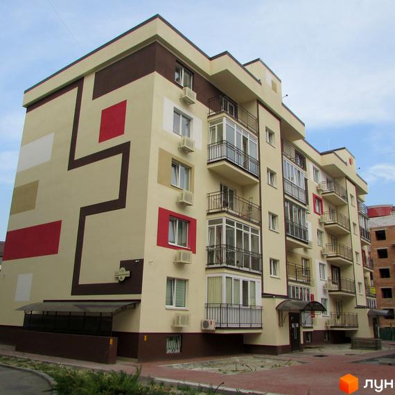 Багатоповерховий будинок Житлового комплексу Голосіївський квартал з бежевим фасадом, коричневими та червоними елементами. Навколо будинку вимощена територія та зелені насадження.