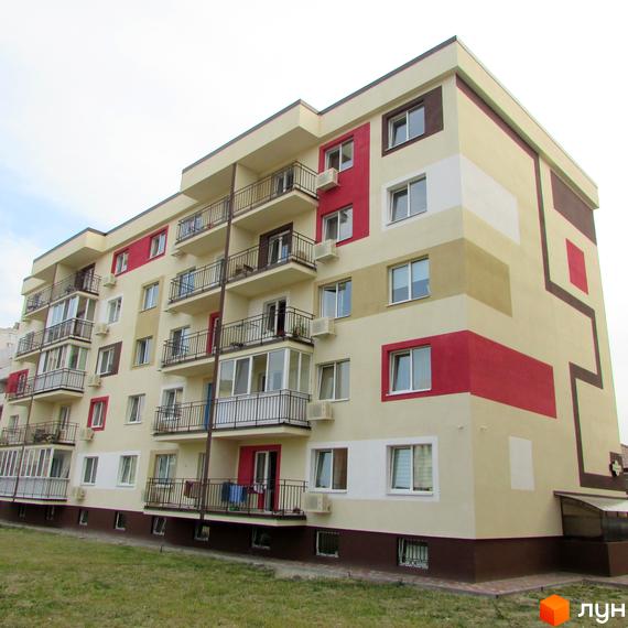 Житловий комплекс Голосіївський квартал: багатоповерховий будинок бежевого кольору з червоними та коричневими акцентами, балконами та вікнами. Перед ним зелений газон.