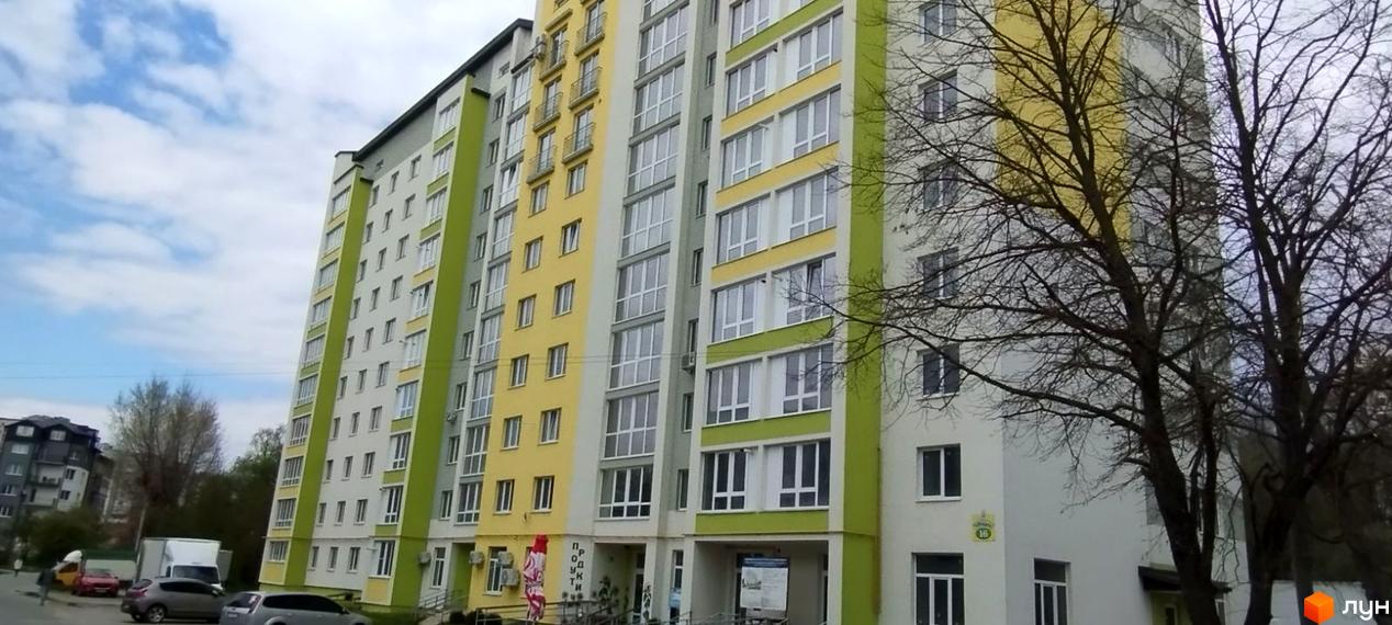 Висотна будівля Житловий комплекс Галичина з великою кількістю вікон. На передньому плані дерева без листя, а також прибудинкова територія з автомобілями.