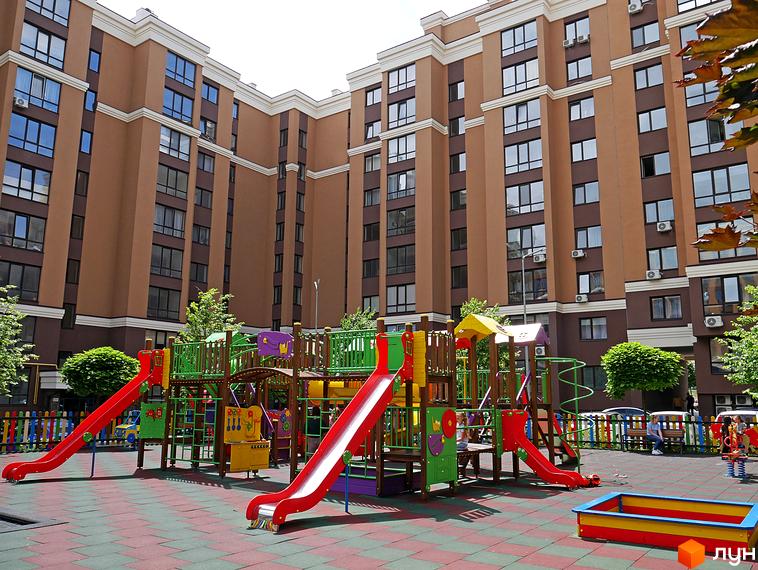 Житловий комплекс Софіївські Липки: багатоповерхові будинки з коричневими фасадами та великими вікнами. Прибудинкова територія облаштована дитячим майданчиком з гірками та пісочницею.