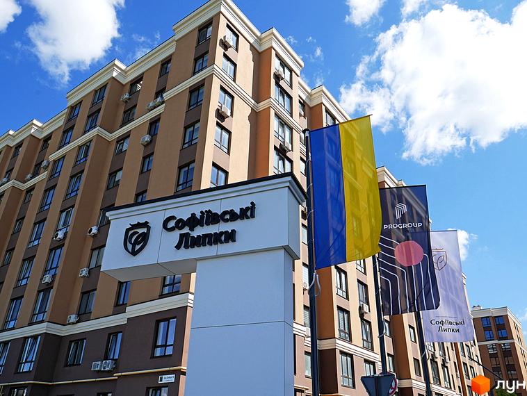 Житловий комплекс Софіївські Липки з фасадом з коричневих та бежевих панелей, вікнами та кондиціонерами. На передньому плані прапори України та компанії PROGROUP.