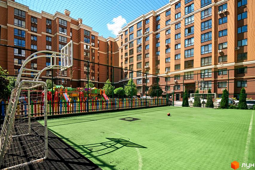 Житловий комплекс Софіївські Липки: цегляні будинки з великими вікнами, спортивний майданчик з покриттям та дитячий майданчик з різнокольоровою огорожею.
