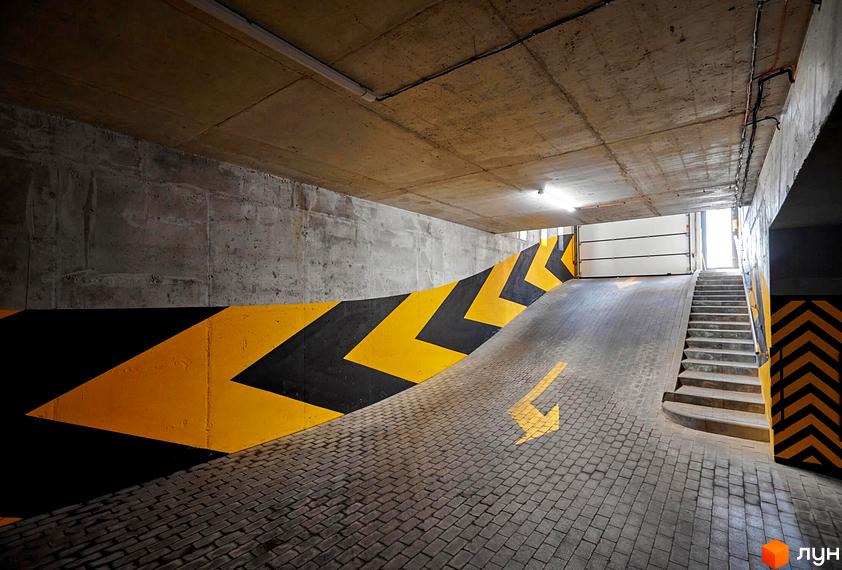 Паркінг у ЖК Софіївські Липки з навігаційними стрілками та сходами. Бетонні стіни та стеля, бруківка на підлозі.