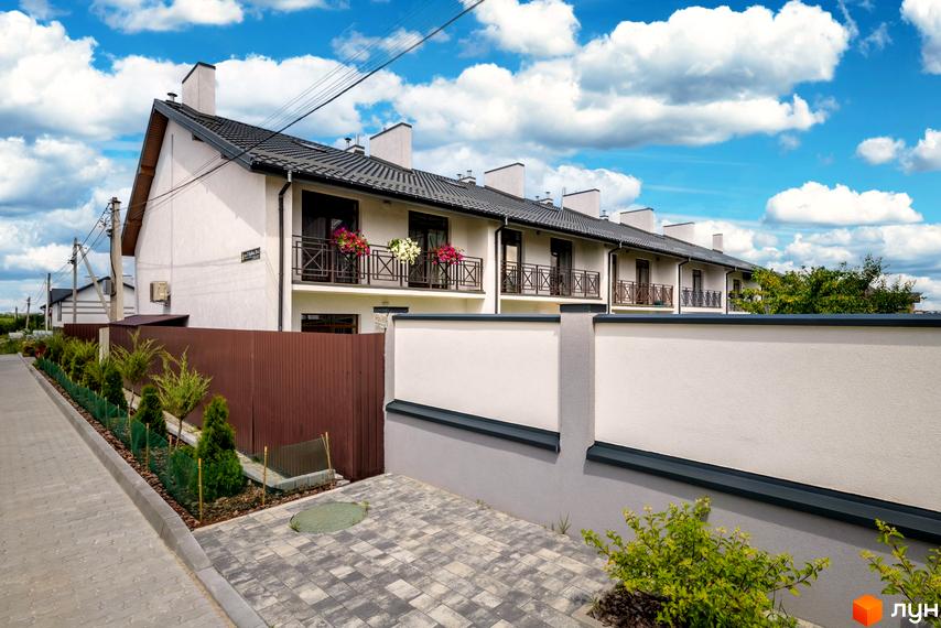 Новобудова з світлими фасадами та темними дахами на вул. Леся Курбаса, 6. Територія облаштована бруківкою та зеленими насадженнями.