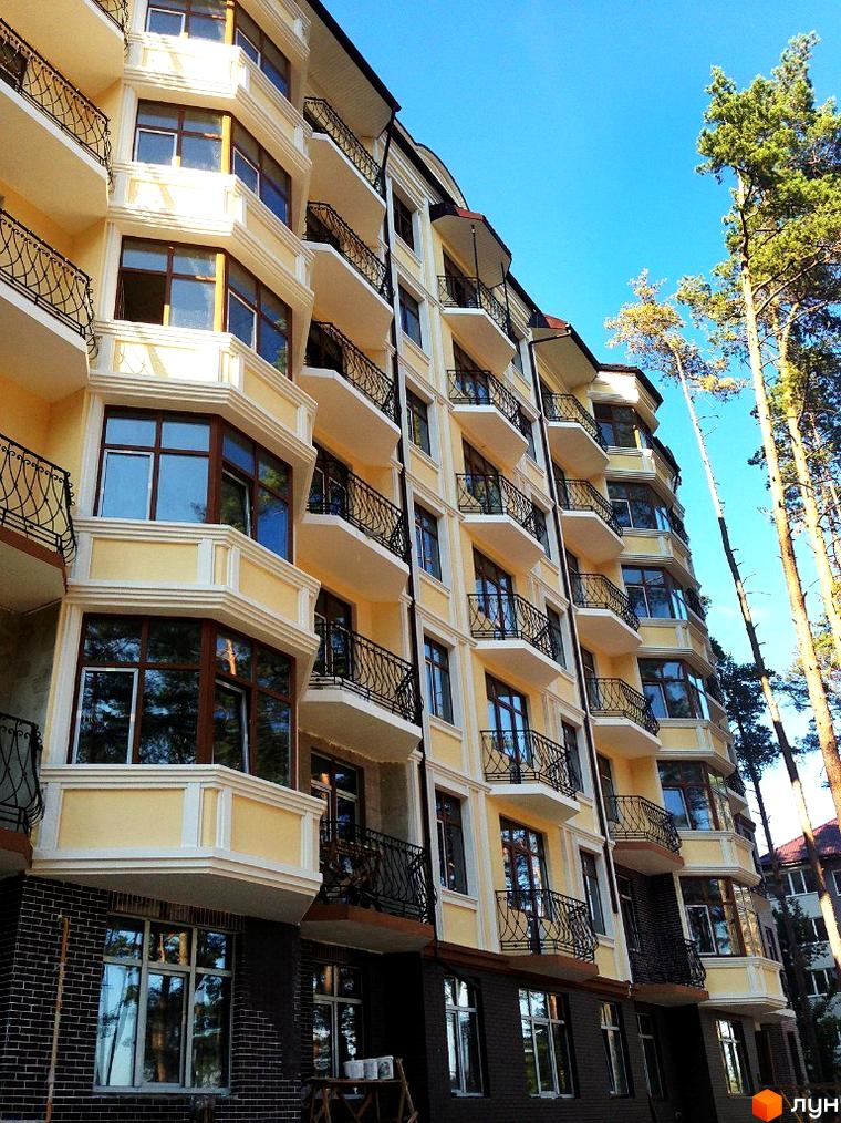 Житловий комплекс Rich Town з балконами та великими вікнами. Поруч ростуть високі дерева, видно блакитне небо.