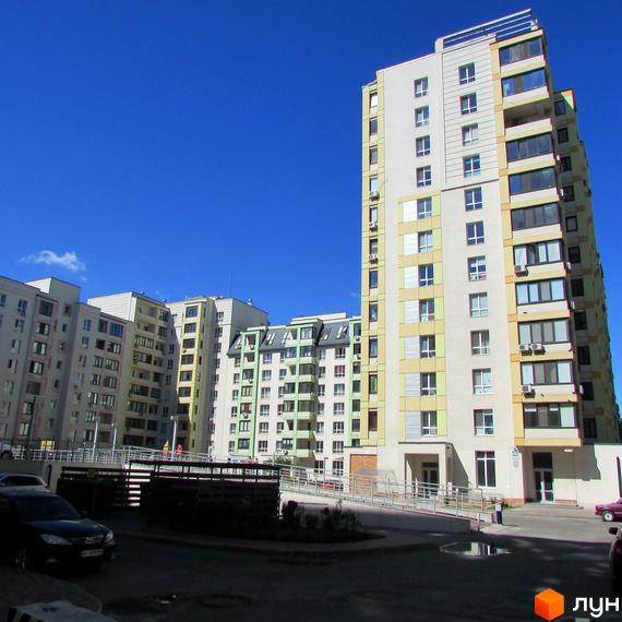 Високі житлові будинки Житлового комплексу Акварелі з фасадами світлих відтінків та численними вікнами. Прибудинкова територія має асфальтований проїзд та пандус.