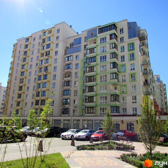 Житловий комплекс Акварелі: багатоповерховий будинок світлого кольору з зеленими та жовтими елементами, парковка та озеленена територія.