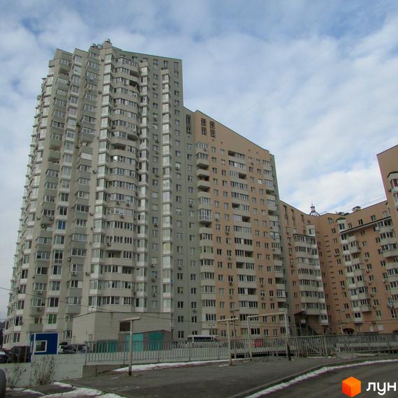 Житловий комплекс Ольжин Град: багатоповерхові будинки світло-сірого та бежевого кольорів з численними вікнами та балконами. На передньому плані дорога та огорожа.