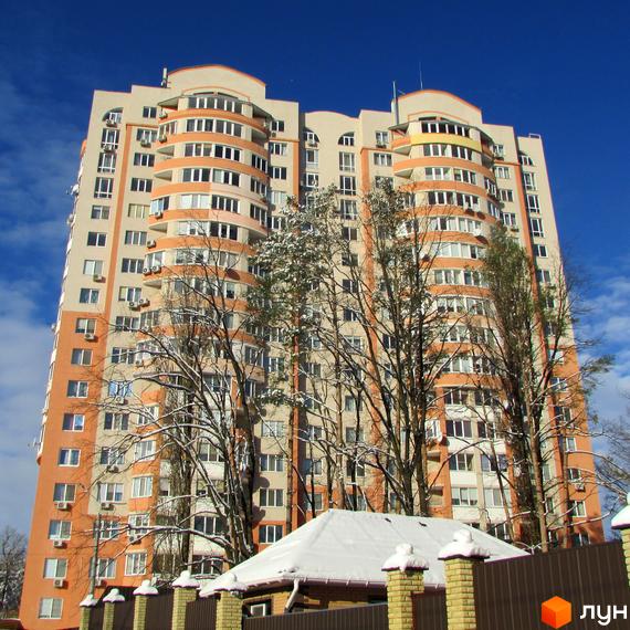 Житловий комплекс Берізки: багатоповерховий будинок світло-бежевого кольору з помаранчевими балконами. На передньому плані засніжені дерева та паркан.