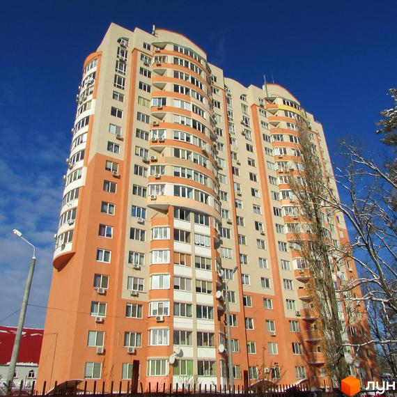 Багатоповерховий житловий будинок Житлового комплексу Берізки з помаранчевими та бежевими фасадами та вигнутою архітектурою. Навколо видно дерева зі снігом та яскраве синє небо.