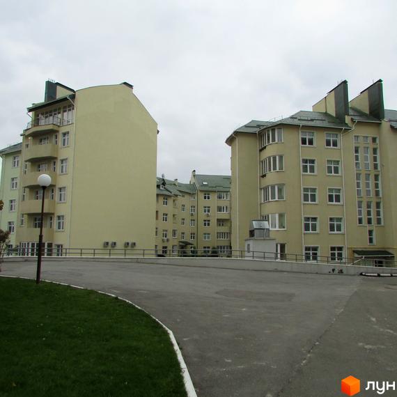 Будівлі Житлового комплексу Петропавлівський зі світлим фасадом та зеленими дахами. На передньому плані асфальтована дорога та доглянутий газон.