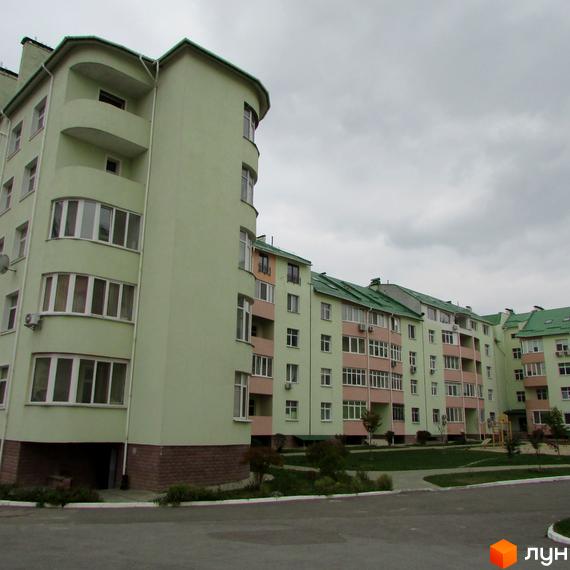Житловий комплекс Петропавлівський: будинки світло-зеленого кольору з рожевими балконами та зеленими дахами. На прибудинковій території є зелені насадження та дитячий майданчик.