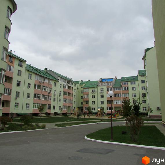 Житловий комплекс Петропавлівський з будинками світло-зеленого кольору та зеленими дахами. На території є асфальтовані доріжки, доглянуті газони та дитячий майданчик.