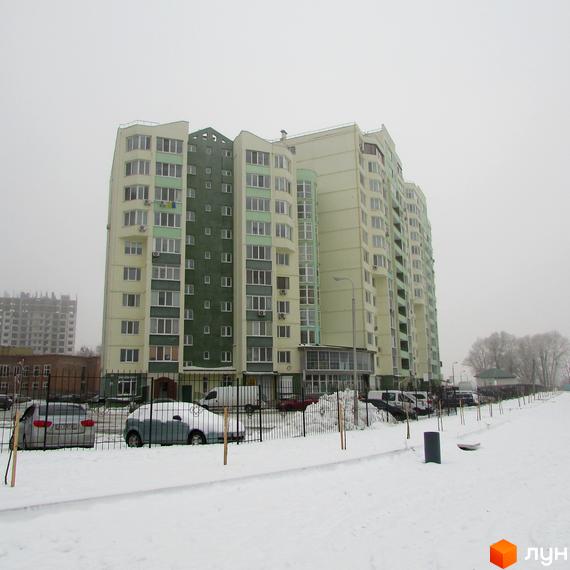 Житловий комплекс Едем з фасадом у світлих тонах та зеленими елементами. Прибудинкова територія засипана снігом з припаркованими автомобілями.