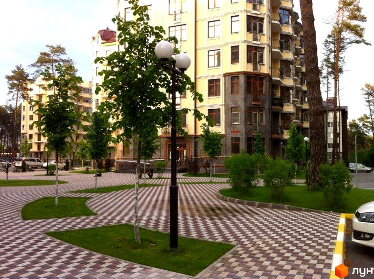 Житловий комплекс Rich Town з фасадом жовтого кольору. На прибудинковій території викладена плитка, є зелені насадження та ліхтарі.