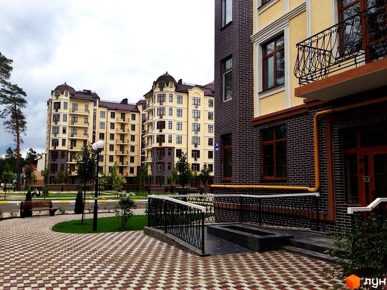 Житловий комплекс Rich Town. Високі будинки з жовтим фасадом та балконами, облицьовані темною цеглою. На передньому плані – бруківка та зелені насадження.