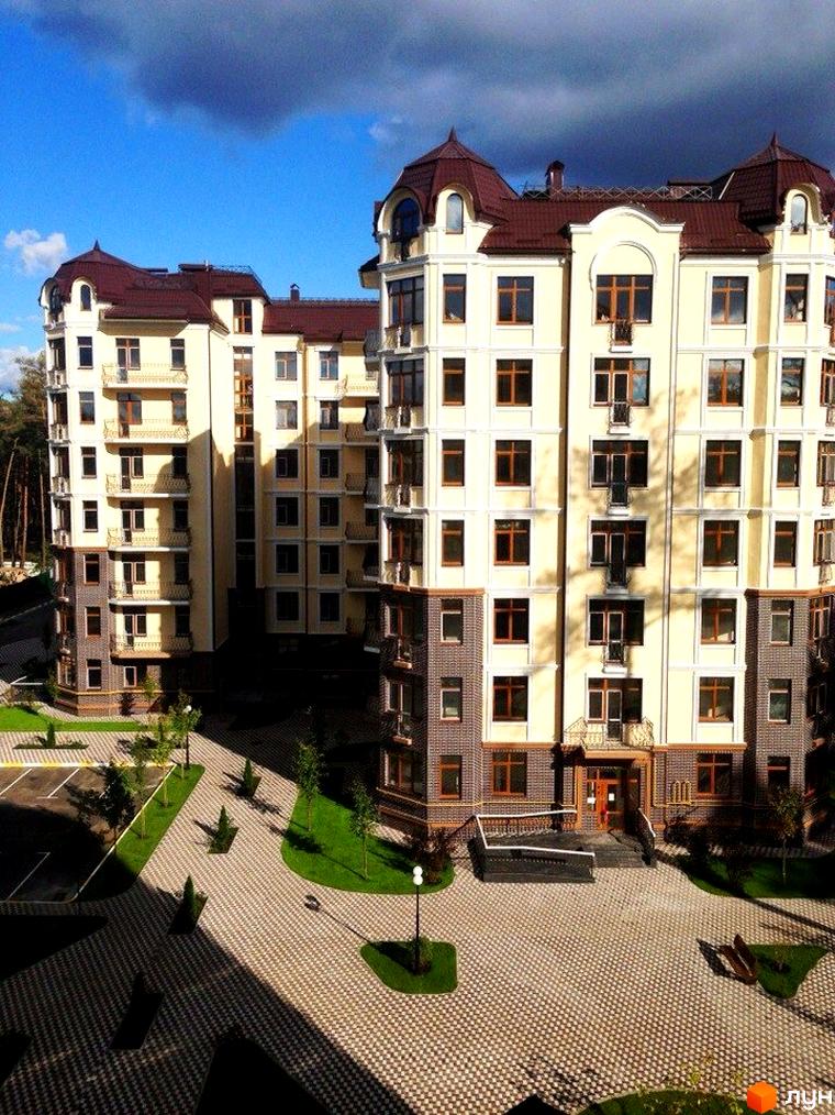 Житловий комплекс Rich Town з фасадами світлих відтінків та коричневим дахом. На території комплексу бруківка, зелені газони та дерева.