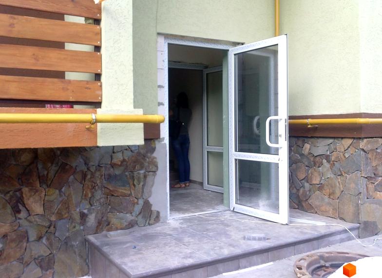 Вхід до будинку житлового комплексу Європейський з відкритими дверима. Прибудинкова територія з плиткою та кам'яною обробкою.