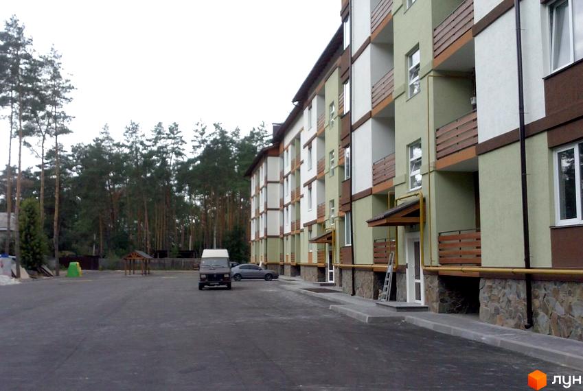 Зображення ЖК Європейський. Багатоквартирний будинок з балконами та фасадом у світлих тонах. На передньому плані асфальтована дорога та прибудинкова територія.