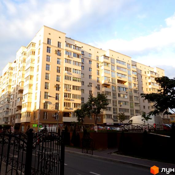 Житловий комплекс Софіївський з фасадом та великими вікнами. Прибудинкова територія з зеленими насадженнями та паркувальними місцями.