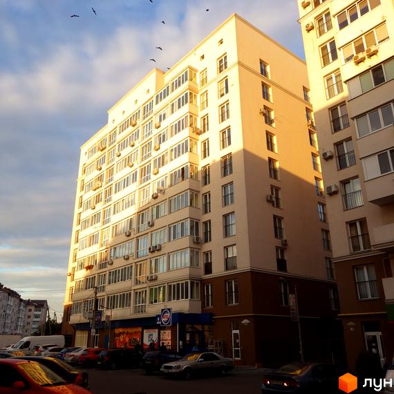 Житловий комплекс Софіївський з сучасним фасадом та прибудинковою територією, де розташовані автомобілі та магазини.