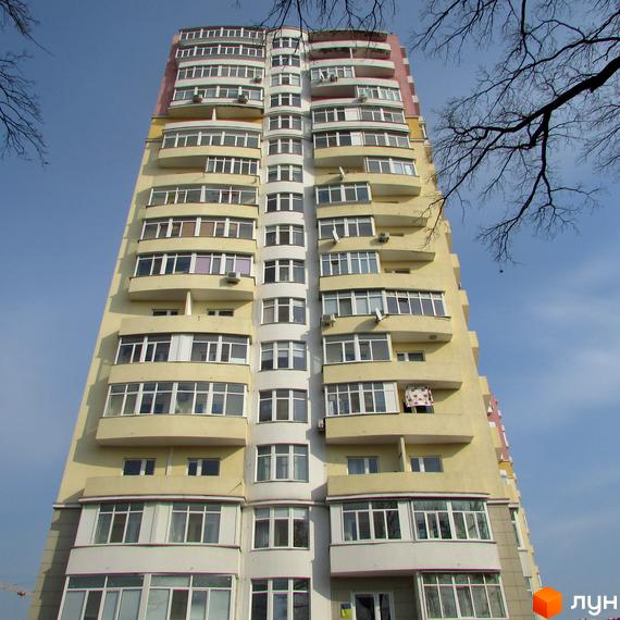 Високий житловий будинок Житлового комплексу Гранд Лайф з фасадом світло-жовтого кольору, білими та рожевими елементами під блакитним небом.