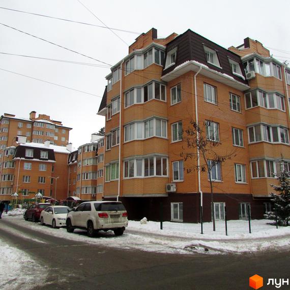 Зовнішній вигляд житлового комплексу ЖК Суворов з цегляною фасадою. Прибудинкова територія з автомобілями та зеленими насадженнями.