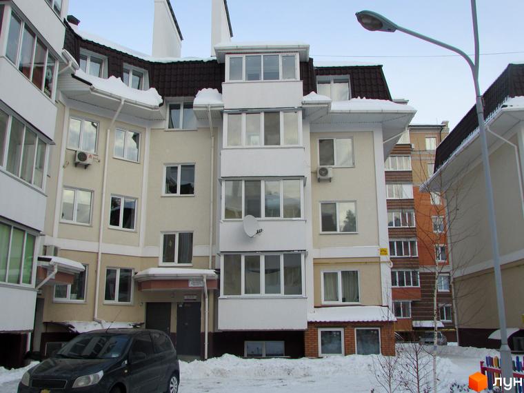 Зовнішній вигляд житлового комплексу Матросова взимку. Будинок має світлий фасад, коричневий дах та багато вікон. Навколо засніжена територія.