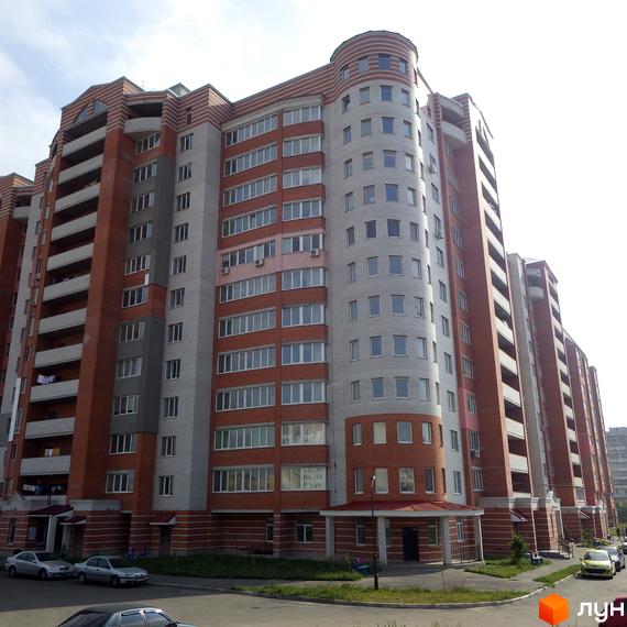 Житловий комплекс ЖК Городок з фасадом у червоній та сірих тонах, прибудинкова територія з автомобілями та зеленими насадженнями.