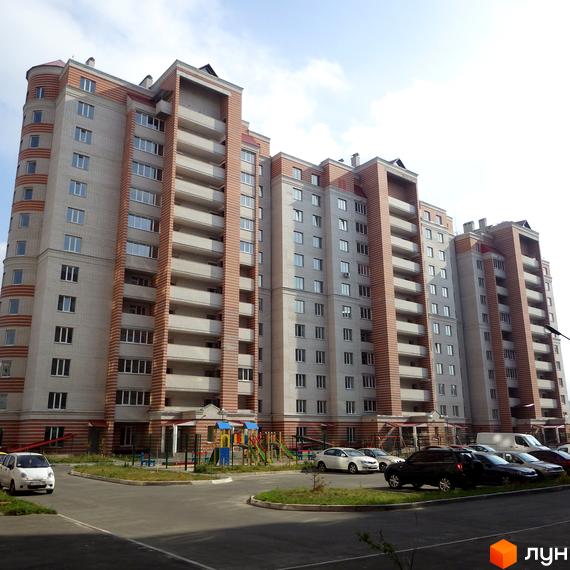 Зовнішній вигляд новобудови ЖК Городок з цегляним оздобленням та балконами. На прибудинковій території розташовані дитячий майданчик та парковка з автомобілями.