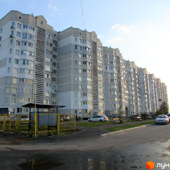 Житловий комплекс Петрівський оновлений з фасадом з білих та сірих панелей. Прибудинкова територія з парковими зонами та автомобілями.