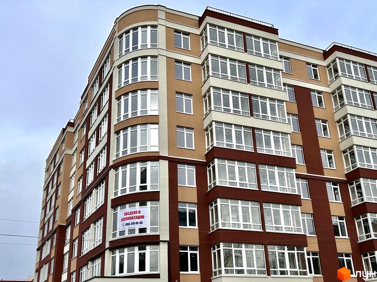 Багатоповерховий будинок ЖК Комфорт з панорамними вікнами та балконами. На фасаді будинку розміщено банер з інформацією про введення в експлуатацію.