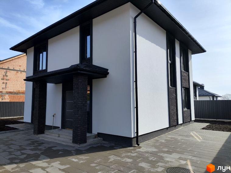 Зображення фасаду та прибудинкової території Котеджного містечка Пейзажі Ірпеня. Двоповерховий будинок з чорними вікнами та білими стінами.