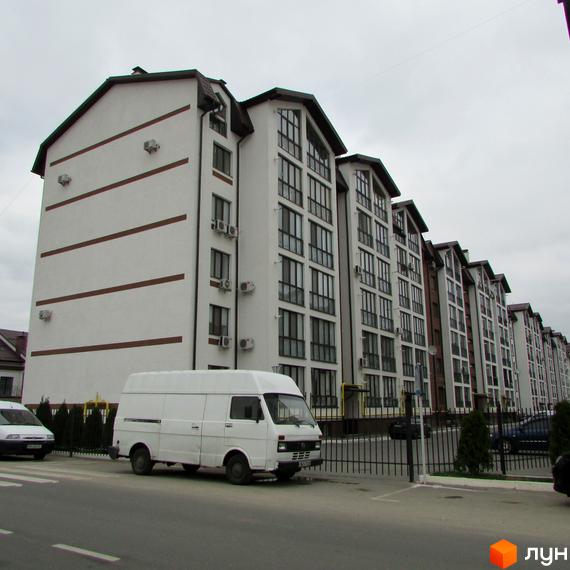 Зовнішній вигляд багатоквартирних будинків ЖК Празький квартал з білими фасадами та темними дахами. Поруч розташована прибудинкова територія з паркуванням та зеленими насадженнями.