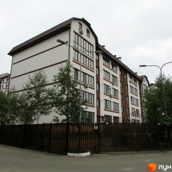 Зовнішній вигляд будинку ЖК Празький квартал з білими та коричневими фасадами, вікнами та кондиціонерами. Огороджена територія з парканом та деревами.