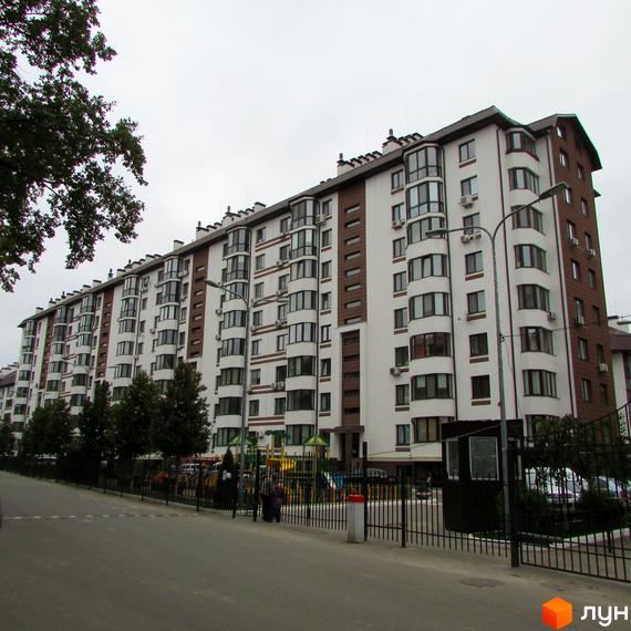 Зовнішній вигляд багатоквартирного будинку ЖК Празький квартал з білими та коричневими фасадами. На прибудинковій території видно дитячий майданчик та огороджену територію.