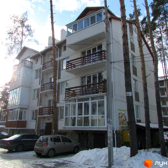 Житловий комплекс Островський: біла багатоповерхова новобудова з дерев'яними балконами та заскленими лоджіями. Прибудинкова територія вкрита снігом, поруч припарковані автомобілі.