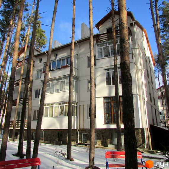 Житловий комплекс Островський. Зовнішній вигляд білої багатоповерхівки серед соснового лісу. На території є лавки та сніг.