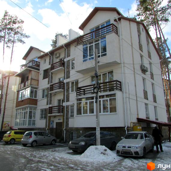 Житловий комплекс Островський – біла багатоповерхова будівля з балконами та великими вікнами. Перед будинком розташована парковка з автомобілями та засніжена територія.