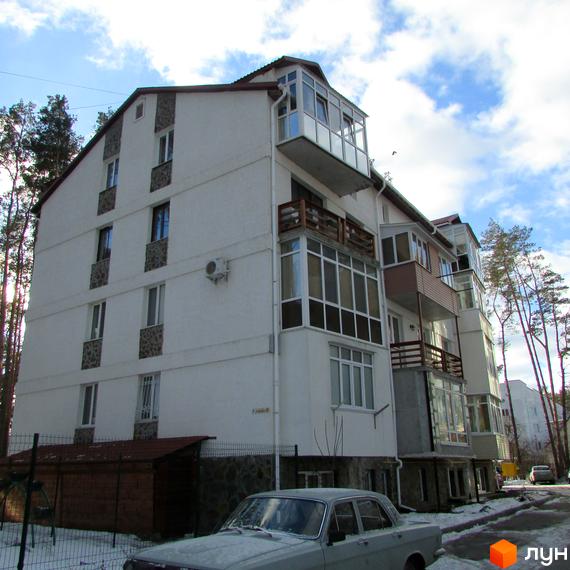 Зовнішній вигляд будинку ЖК Островський з балконами та вікнами. Навколо будинку дерева та засніжена територія.