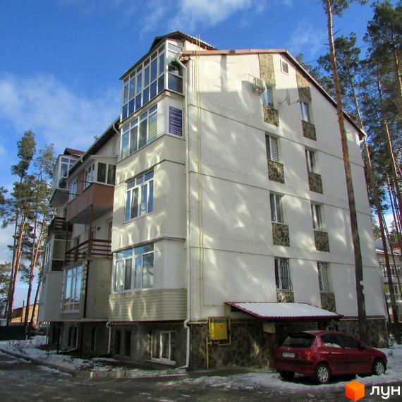 Житловий комплекс Островський – багатоповерхова новобудова з заскленими балконами та кам'яним оздобленням цоколя. Навколо будинку дерева та парковка з червоним автомобілем.