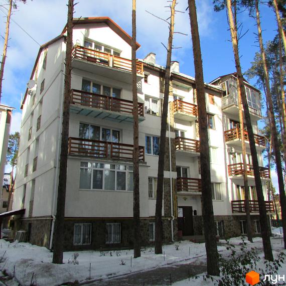 Зовнішній вигляд житлового комплексу Островський з балконами та вікнами. Навколо будинку ростуть дерева, а територія вкрита снігом.