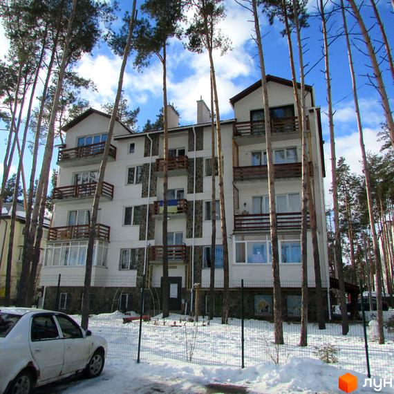 Житловий комплекс Островський: біла багатоповерхівка з балконами серед сосен, зимовий пейзаж з парканом та автомобілем.