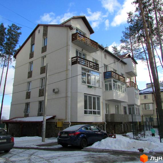 Зовнішній вигляд багатоквартирного будинку ЖК Островський з балконами та вікнами. Навколо будинку видно дерева та засніжену територію.