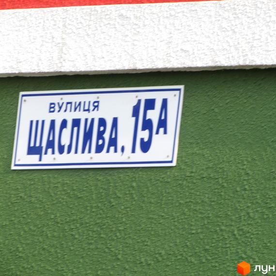 Табличка з назвою вулиці Щаслива, 15А на зеленій стіні. Опис новобудови ЖК Щасливий для просування сайту.